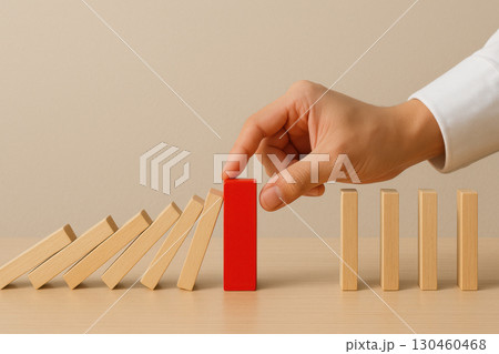 Hand stopping falling wooden dominoes using red block symbolizes risk prevention and decision control in business crisis 130460468