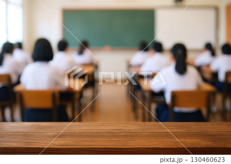 Blurred classroom background with students in uniform sitting at desks, wooden surface in foreground, creating educational atmosphere 130460623