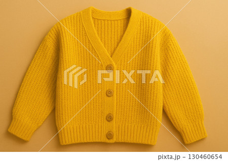 Cozy knitted yellow cardigan with wooden buttons on warm beige backdrop, perfect for autumn fashion and soft textile product presentation 130460654
