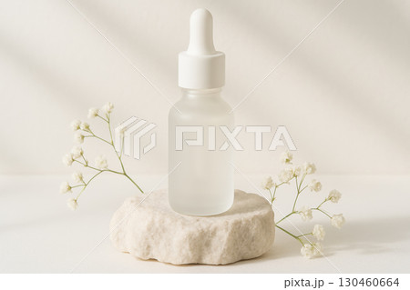 Frosted white serum bottle on bright limestone rock with baby breath flowers, luxury skincare product in daylight, minimal aesthetic 130460664