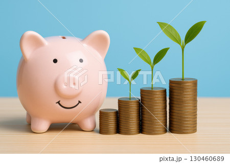 Smiling piggy bank beside coin stacks with sprouting plants symbolizes savings and financial growth against blue background 130460689