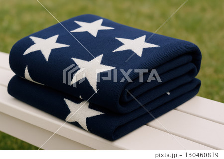 Folded navy blue blanket with white stars on white bench, perfect for Fourth of July picnic or summer event, evoking festive vibe Folded navy blue blanket with white stars on white bench, perfect for Fourth of July picnic or summer event, evoking festive vibe 130460819