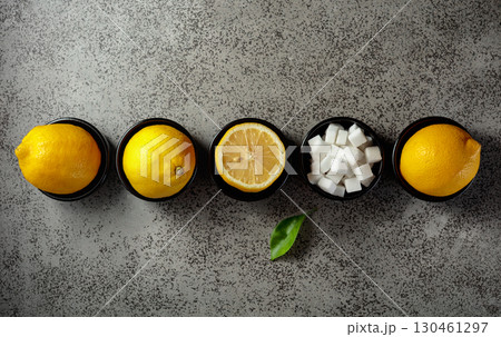Fresh, juicy lemons and sugar cubes in small black bowls on a gray stone table. Fresh, juicy lemons and sugar cubes in small black bowls on a gray stone table. 130461297