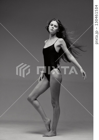 Black and white slender woman posing in a black bodysuit with a neutral expression in a studio setting 130461584