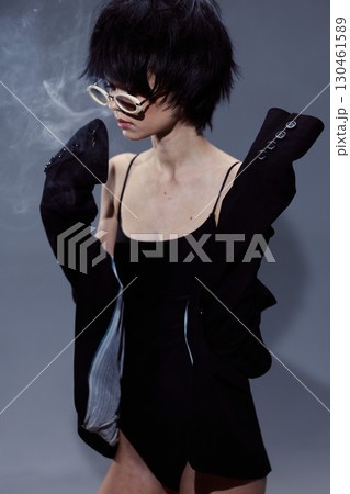 stylish woman with glasses wearing black clothing in moody lighting with smoky background and dramatic pose 130461589