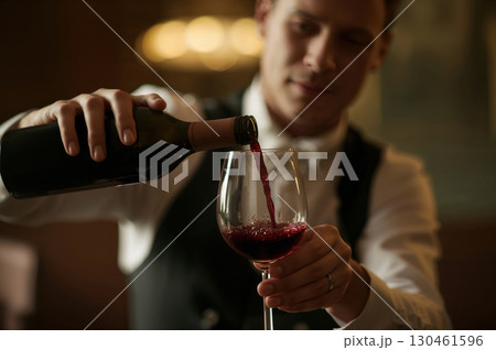 Sommelier pours luxurious wine with refined grace in warm cellar setting Sommelier pours luxurious wine with refined grace in warm cellar setting 130461596