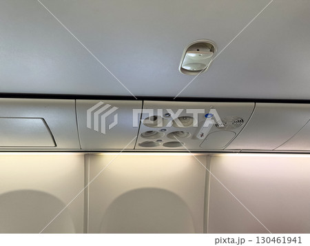An airplane cabin ceiling with air vents, signs, and compartments above the passenger seats. Travel, aviation, and the technical design of aircraft interiors for comfort and safety. 130461941