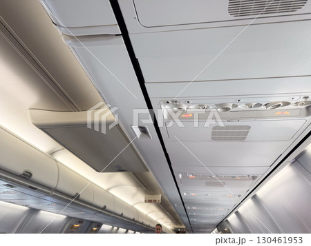 An airplane cabin ceiling with air vents, signs, and compartments above the passenger seats. Travel, aviation, and the technical design of aircraft interiors for comfort and safety. An airplane cabin ceiling with air vents, signs, and compartments above the passenger seats. Travel, aviation, and the technical design of aircraft interiors for comfort and safety. 130461953