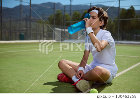 Young Tennis Player Resting and Rehydrating During Outdoor Training Session 130462259