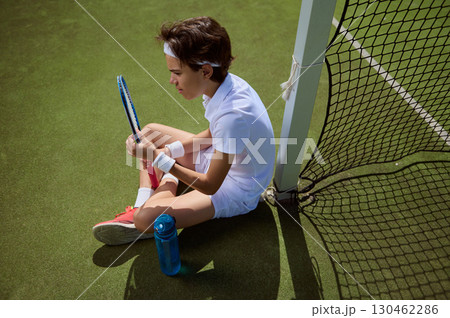 Focused Young Tennis Player Sitting on Court by the Net Outdoors 130462286