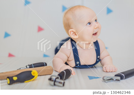 Adorable baby in a mechanic costume surrounded by toy tools. Concept of repair, imaginative play, and introducing kids to the world of fixing and problem-solving through fun 130462346