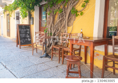 Outdoor cafe with rustic wooden tables and chairs set against a yellow wall adorned with climbing vines. A chalkboard menu adds charm to the inviting atmosphere. 130463005
