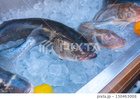 Fresh fish are displayed on a bed of ice, showcasing various species including bass, with lemon accents. The market setting emphasizes freshness and quality, ideal for seafood enthusiasts. 130463008