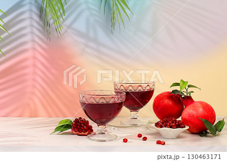 Red pomegranate wine and grains with ripe pomegranates on a trendy table with palm shades, concept festive party, advertising for a bar and cafe. Source of vitamins for a healthy lifestyle, 130463171