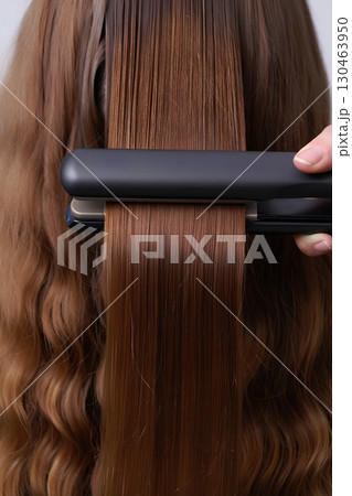 Close-up of flat iron straightening long hair, beauty salon tool in action , haircare and styling routine concept 130463950