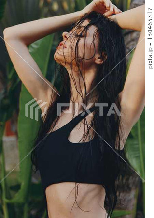 Tropical beauty Woman in black bikini top posing by palm tree with windblown hair under sunny skies Tropical beauty Woman in black bikini top posing by palm tree with windblown hair under sunny skies 130465317