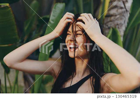 Happy young woman in stylish black swimsuit smiling and holding her hair up in the air on the beach 130465319