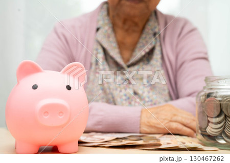 Retired elderly woman counting coins money with piggy bank and worry about monthly expenses and treatment fee payment. 130467262
