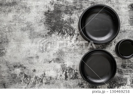 Minimalist arrangement of three black ceramic bowls on a textured surface in natural lighting 130469258