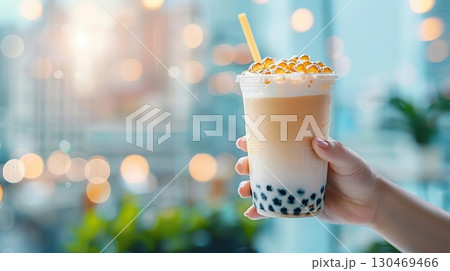 Closeup of a hand holding a cup of bubble tea with a city skyline in the background. Closeup of a hand holding a cup of bubble tea with a city skyline in the background. 130469466