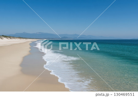 Sunny beach with clear waters and distant mountains on a calm day in a coastal paradise 130469551