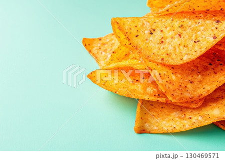 Crunchy tortilla chips stacked on a turquoise background with spicy seasoning for snack time enjoyment 130469571