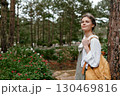 Young woman in casual outfit with a backpack, smiling outdoors surrounded by greenery and flowers, capturing a serene moment in nature 130469816