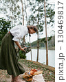 Young woman in nature with green skirt and white blouse, joyfully organizing autumn leaves near a river, evoking a sense of connection to nature and seasonal change 130469817