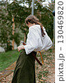 A young woman in a white blouse and long olive skirt stands outdoors, embodying a serene autumn mood with nature s backdrop, showcasing emotional connection to fashion 130469820