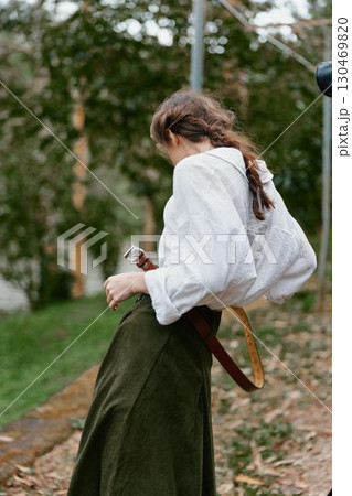 A young woman in a white blouse and long olive skirt stands outdoors, embodying a serene autumn mood with nature s backdrop, showcasing emotional connection to fashion A young woman in a white blouse and long olive skirt stands outdoors, embodying a serene autumn mood with nature s backdrop, showcasing emotional connection to fashion 130469820