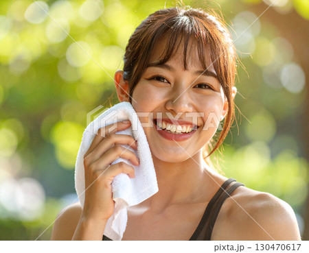 タオルで汗を拭く若い女性/ Young woman wiping sweat with a towe 130470617