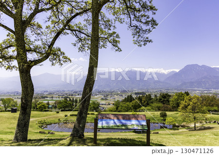 木陰から眺めるあづみ野池田クラフトパークと北アルプスの春景色 木陰から眺めるあづみ野池田クラフトパークと北アルプスの春景色 130471126