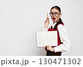 surprised girl with open notebook and pen, wearing glasses, standing against a light gray background, dressed in a red vest and white shirt, showing excitement in her expression 130471302
