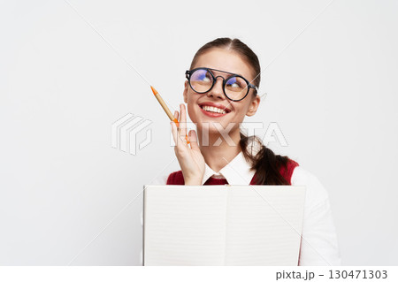 Smiling student with glasses holding a notebook and a pencil, looking thoughtful against a white background Engaging expression indicating creativity and inspiration 130471303