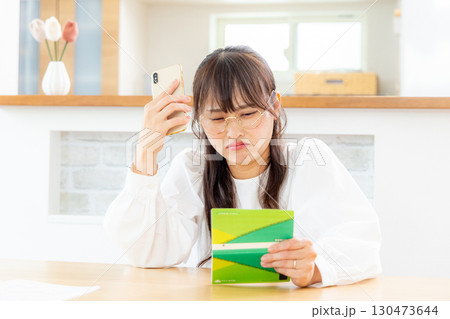 預金通帳を見て悩む女性 預金通帳を見て悩む女性 130473644