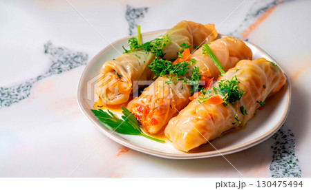 macro photo of cabbage rolls decorated with greens in a plate on a white marble serving tabl 130475494