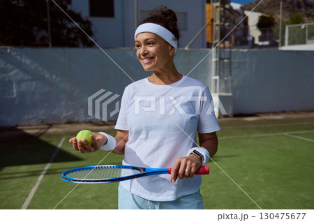 Active Woman Smiling on a Tennis Court Holding Racket and Ball 130475677