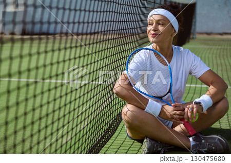 Woman Resting on Tennis Court While Holding a Racket 130475680