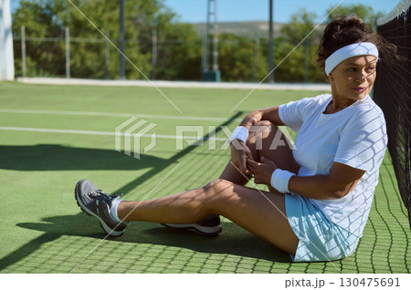 Female Tennis Player Resting Thoughtfully Next to a Net on a Sunny Court 130475691
