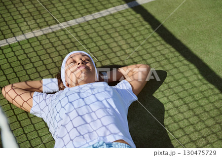 Relaxed Athlete Lying on Grass with Shadows from Tennis Net Relaxed Athlete Lying on Grass with Shadows from Tennis Net 130475729