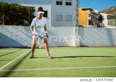 Woman Playing Tennis Outdoors on a Sunny Day with Background Houses 130475980