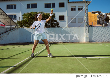 Female Tennis Player Preparing to Serve on Sunny Outdoor Court Female Tennis Player Preparing to Serve on Sunny Outdoor Court 130475997