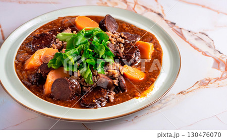 Feijoada garnished with greens in a plate on a white marble serving table 130476070