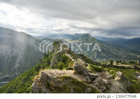 The ruins of a stone fortress sit atop a rocky mountain ridge with green valleys down below 130477046