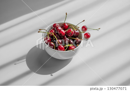 Bowl with fresh red cherry on white background with sunny light and shadows. Bowl with fresh red cherry on white background with sunny light and shadows. 130477071