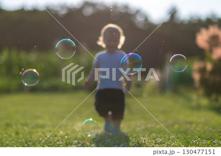 Child playing with bubbles in a sunlit outdoor setting during a warm afternoon Child playing with bubbles in a sunlit outdoor setting during a warm afternoon 130477151