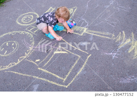 Little child creating colorful chalk art on pavement while sitting outside on a sunny day 130477152