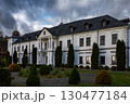 Elegant white mansion surrounded by manicured gardens under a dramatic sky during late afternoon 130477184