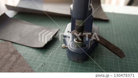 Close up of leather strap placed under press machine in workshop for handmade accessory production Close up of leather strap placed under press machine in workshop for handmade accessory production 130478371