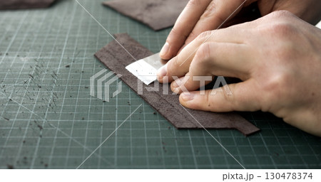 Craftsman skiving surface of leather strip with blade tool on green cutting mat in workshop Craftsman skiving surface of leather strip with blade tool on green cutting mat in workshop 130478374